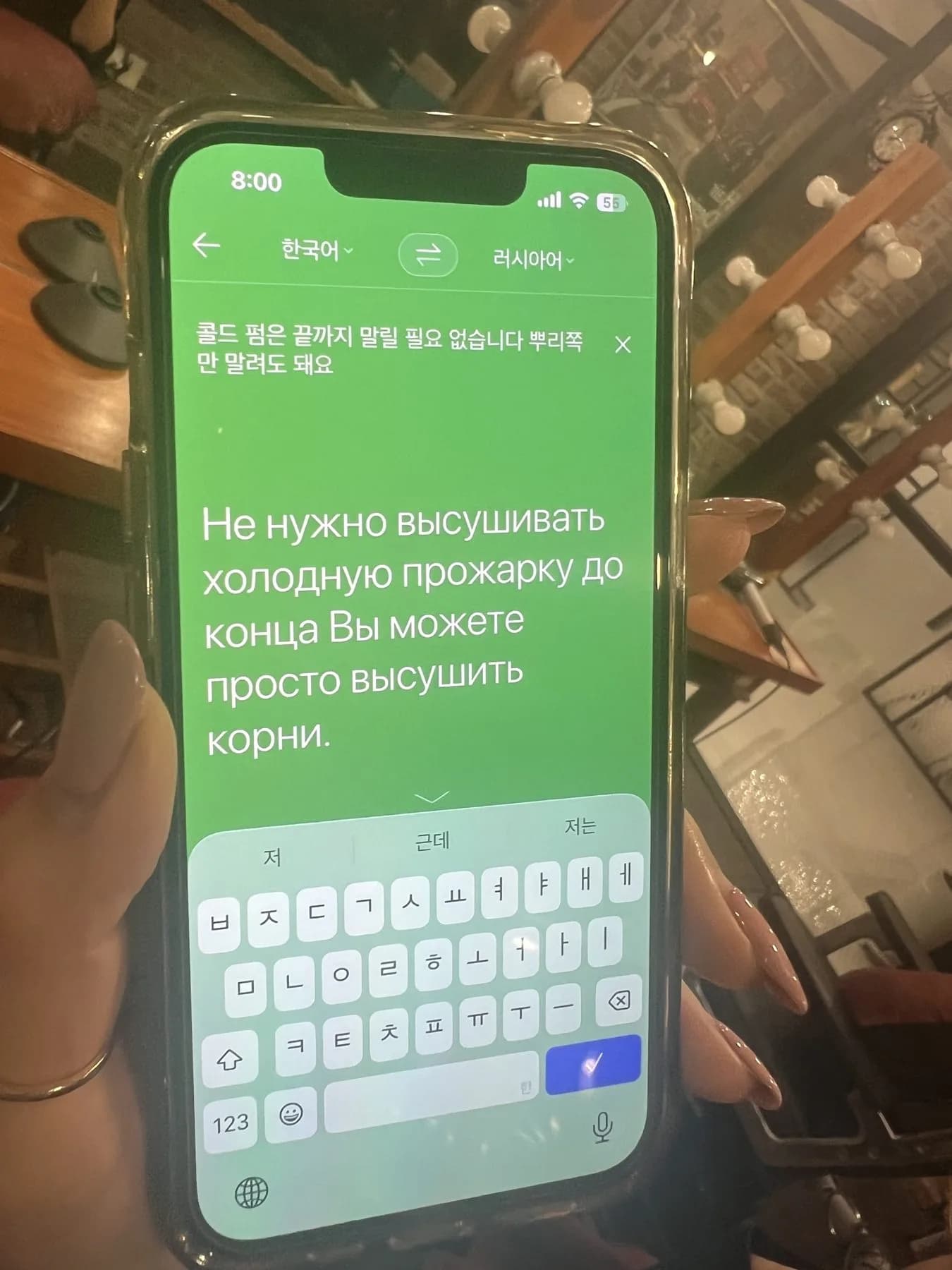 Phone with a translation app showing a Korean phrase about cold perm and its Russian translation
